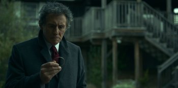 Movie still from “Lost Girls” (2020), directed by Liz Garbus – An older man wearing a suit and tie holding a pair of eyeglasses; Close Up shot, Over the shoulder angle