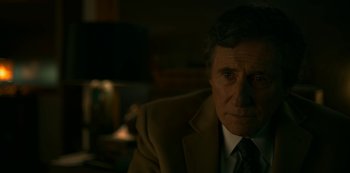 Movie still from “Lost Girls” (2020), directed by Liz Garbus – An older man wearing a suit and tie in a dark room; Close Up shot, Over the shoulder angle