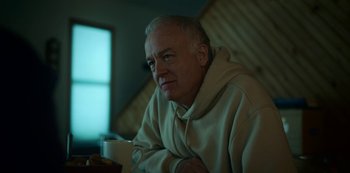 Movie still from “Lost Girls” (2020), directed by Liz Garbus – An older man sitting at a table with a cup of coffee; Close Up shot, Low angle