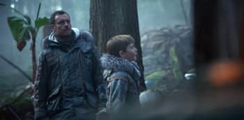 Movie still from “Lost in Space” (2018), created by Irwin Allen – A man and a boy are standing next to each other; Medium shot, Over the shoulder angle