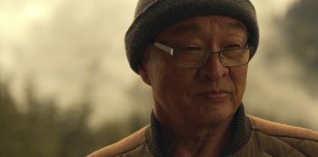Movie still from “Lost in Space” (2018), created by Irwin Allen – An older man wearing glasses and a hat; Close Up shot, Over the shoulder angle