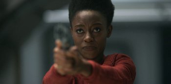 Movie still from “Lost in Space” (2018), created by Irwin Allen – A woman is holding a gun in her hand; Close Up shot, Over the shoulder angle