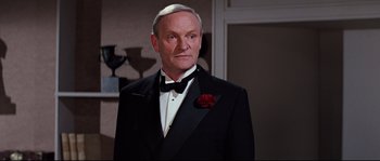 Movie still from “Indiana Jones and the Last Crusade” (1989), directed by Steven Spielberg – An older man in a tuxedo with a red flower in his lapel; Medium shot, Low angle