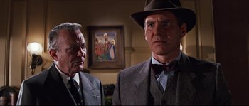 Movie still from “Indiana Jones and the Last Crusade” (1989), directed by Steven Spielberg – A man in a suit and a hat standing next to another man in a suit and a hat; Close Up shot, Low angle