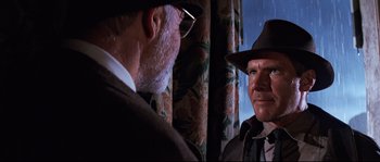 Movie still from “Indiana Jones and the Last Crusade” (1989), directed by Steven Spielberg – A man in a suit and a man in a hat; Close Up shot, Over the shoulder angle