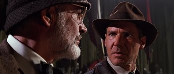 Movie still from “Indiana Jones and the Last Crusade” (1989), directed by Steven Spielberg – A man in a hat and a man in a suit and tie; Close Up shot, Over the shoulder angle