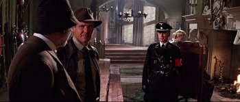 Movie still from “Indiana Jones and the Last Crusade” (1989), directed by Steven Spielberg – A man and a man in uniform standing next to each other in front of a building; Medium shot, Over the shoulder angle