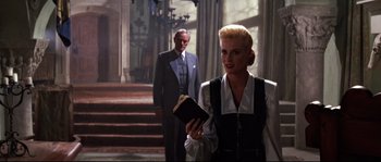 Movie still from “Indiana Jones and the Last Crusade” (1989), directed by Steven Spielberg – A man and a woman standing next to each other in front of a staircase; Medium shot, Low angle