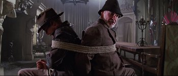 Movie still from “Indiana Jones and the Last Crusade” (1989), directed by Steven Spielberg – A man tied to a chair with a rope around his neck; Medium shot, Low angle