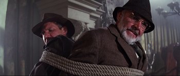 Movie still from “Indiana Jones and the Last Crusade” (1989), directed by Steven Spielberg – A man in a suit and a man in a hat and a rope; Close Up shot, Low angle