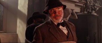 Movie still from “Indiana Jones and the Last Crusade” (1989), directed by Steven Spielberg – An older man wearing a hat and a bow tie; Close Up shot, Over the shoulder angle