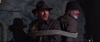 Movie still from “Indiana Jones and the Last Crusade” (1989), directed by Steven Spielberg – A man wearing a hat and a rope around his neck; Medium shot, Low angle