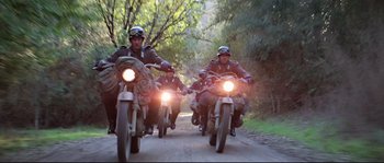 Movie still from “Indiana Jones and the Last Crusade” (1989), directed by Steven Spielberg – A group of men riding motorcycles down a dirt road; Wide shot, Low angle