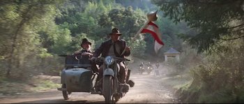 Movie still from “Indiana Jones and the Last Crusade” (1989), directed by Steven Spielberg – A group of people riding on the back of a motorcycle; Wide shot, Low angle