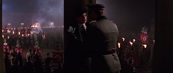 Movie still from “Indiana Jones and the Last Crusade” (1989), directed by Steven Spielberg – A man and a woman standing next to each other in front of a crowd; Medium shot, Over the shoulder angle