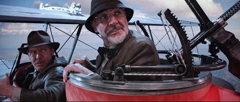 Movie still from “Indiana Jones and the Last Crusade” (1989), directed by Steven Spielberg – An older man in a hat and glasses sitting in an airplane; Close Up shot, Low angle