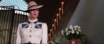 Movie still from “Indiana Jones and the Last Crusade” (1989), directed by Steven Spielberg – A woman wearing a hat standing in front of a staircase; Medium shot, Low angle