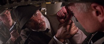 Movie still from “Indiana Jones and the Last Crusade” (1989), directed by Steven Spielberg – An older man wearing a hat and glasses holding a pair of scissors in his hand; Close Up shot, Low angle