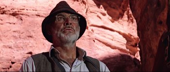 Movie still from “Indiana Jones and the Last Crusade” (1989), directed by Steven Spielberg – An older man wearing a hat and glasses in front of a rock wall; Close Up shot, Low angle