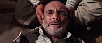 Movie still from “Indiana Jones and the Last Crusade” (1989), directed by Steven Spielberg – An older man with glasses is being held by a woman; Close Up shot, Overhead angle