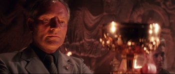 Movie still from “Indiana Jones and the Last Crusade” (1989), directed by Steven Spielberg – An older man in a suit and tie in front of a chandelier; Close Up shot, Low angle