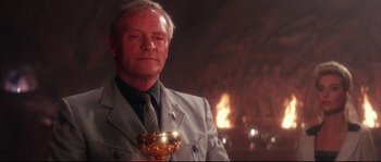 Movie still from “Indiana Jones and the Last Crusade” (1989), directed by Steven Spielberg – An older man holding a goblet in front of a fire; Close Up shot, Low angle
