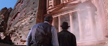 Movie still from “Indiana Jones and the Last Crusade” (1989), directed by Steven Spielberg – Two men in vests and hats looking at a building; Wide shot, Low angle