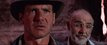 Movie still from “Indiana Jones and the Last Crusade” (1989), directed by Steven Spielberg – A man and a woman standing next to each other; Close Up shot, Over the shoulder angle