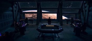 Movie still from “Lost in Space” (2018), created by Irwin Allen – A man sitting in front of a large screen in a room; Extreme Wide shot, High angle