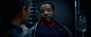 Movie still from “Lost in Space” (2018), created by Irwin Allen – A man in a black and red jacket talking to another man; Close Up shot, Over the shoulder angle