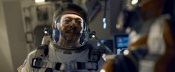 Movie still from “Lost in Space” (2018), created by Irwin Allen – A man in a spacesuit and a helmet is smiling; Close Up shot, Over the shoulder angle