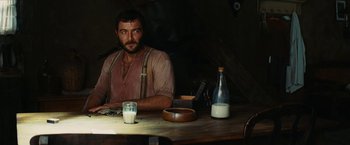 Movie still from “Inglourious Basterds” (2009), directed by Quentin Tarantino – A man sitting at a wooden table with a glass of milk; Medium shot, High angle