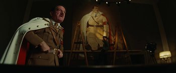 Movie still from “Inglourious Basterds” (2009), directed by Quentin Tarantino – A man standing in front of a painting of adolf hitler; Medium shot, Low angle