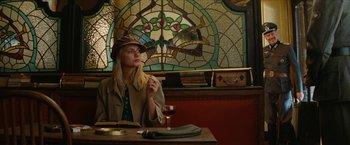 Movie still from “Inglourious Basterds” (2009), directed by Quentin Tarantino – A woman sitting at a table in front of a stained - glass window; Medium shot, Low angle