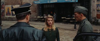 Movie still from “Inglourious Basterds” (2009), directed by Quentin Tarantino – A woman standing in front of a man in front of a building; Medium shot, Over the shoulder angle