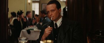 Movie still from “Inglourious Basterds” (2009), directed by Quentin Tarantino – A man smoking a cigarette in front of a group of people; Close Up shot, Over the shoulder angle