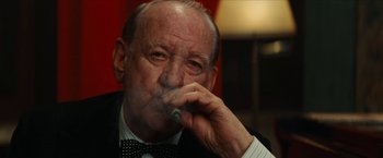 Movie still from “Inglourious Basterds” (2009), directed by Quentin Tarantino – An older man smoking a cigarette while wearing a bow tie; Close Up shot, Low angle