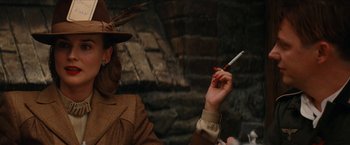 Movie still from “Inglourious Basterds” (2009), directed by Quentin Tarantino – A person holding a cigarette in their hand and wearing a hat; Close Up shot, Over the shoulder angle