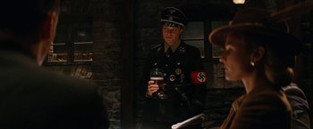 Movie still from “Inglourious Basterds” (2009), directed by Quentin Tarantino – A man in a nazi uniform holding a glass of beer; Medium shot, Over the shoulder angle