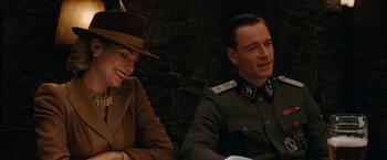 Movie still from “Inglourious Basterds” (2009), directed by Quentin Tarantino – A man and a woman sitting next to each other in front of a brick wall; Medium shot, Over the shoulder angle