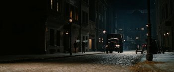 Movie still from “Inglourious Basterds” (2009), directed by Quentin Tarantino – A street scene with a bus and people walking on the sidewalk at night; Extreme Wide shot, High angle