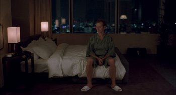 Movie still from “Lost in Translation” (2003), directed by Sofia Coppola – A man sitting on top of a bed in front of a window at night; Wide shot, High angle