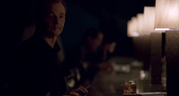 Movie still from “Lost in Translation” (2003), directed by Sofia Coppola – An older man sitting at a table with a glass of whiskey; Close Up shot, Over the shoulder angle