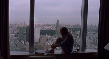 Movie still from “Lost in Translation” (2003), directed by Sofia Coppola – A woman sitting in front of a large window looking out at a city skyline; Wide shot, High angle