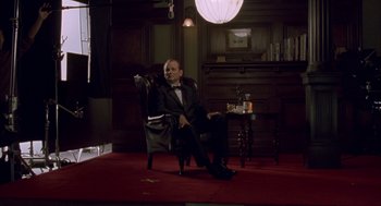 Movie still from “Lost in Translation” (2003), directed by Sofia Coppola – A man sitting in a chair in front of a table; Wide shot, Low angle