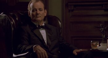 Movie still from “Lost in Translation” (2003), directed by Sofia Coppola – A man sitting in a chair wearing a suit and bow tie; Medium shot, Low angle