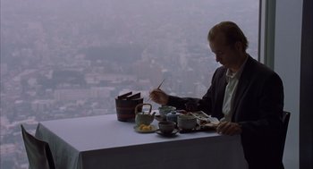 Movie still from “Lost in Translation” (2003), directed by Sofia Coppola – A man sitting at a table with a plate of food in front of him; Medium shot, Low angle