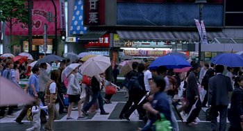 Movie still from “Lost in Translation” (2003), directed by Sofia Coppola – A group of people walking across a crosswalk holding umbrellas; Extreme Wide shot, High angle