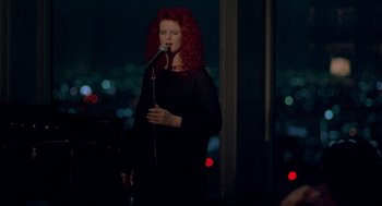 Movie still from “Lost in Translation” (2003), directed by Sofia Coppola – A woman with long red curly hair holding a microphone in front of a window; Medium shot, High angle