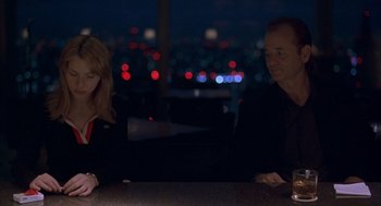 Movie still from “Lost in Translation” (2003), directed by Sofia Coppola – A man and a woman sitting at a table in front of a city skyline; Medium shot, High angle